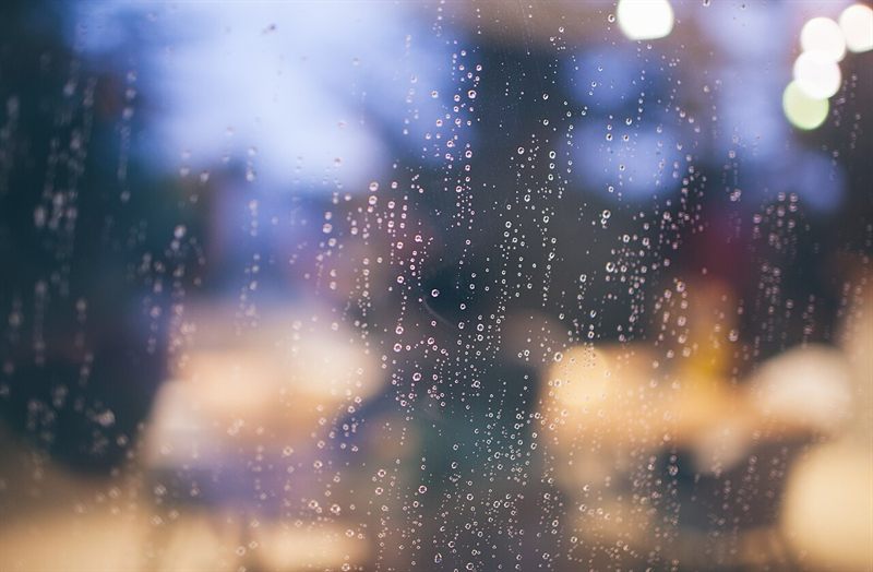 Raindrops on a cafe window with warm lamps and tables blurred behind the glass