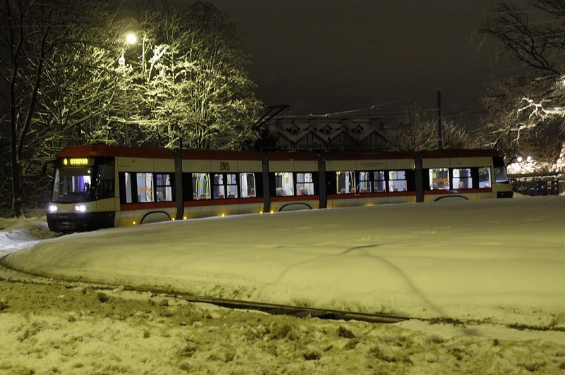 Tram with lit windows on a snow-covered loop under a street lamp at night