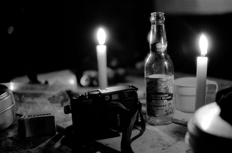 Black-and-white photograph of a rangefinder camera, a box of film and two candles on a wooden hut table